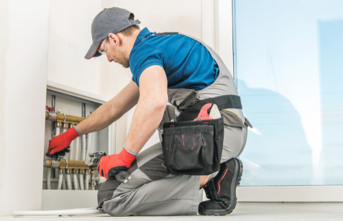 טכנאי אינסטלציה או מומחה בדק בית בודק בזהירות מערכת צנרת סמויה בקיר, מדגיש בדיקת רטיבות ואיתור ליקויים בתשתיות המים.